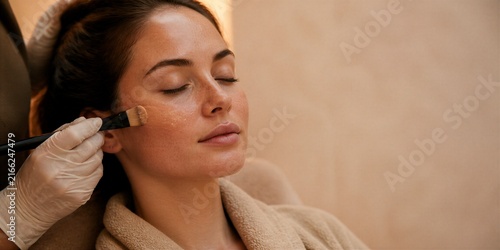 Woman receiving facial treatment with cosmetic brush.