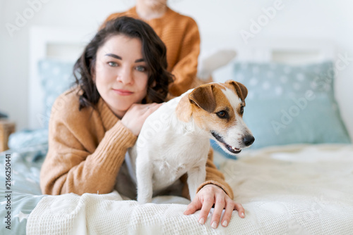 Bild auf Leinwand Close up portrait of a young caucasian brunette woman embracing her jack russell terrier on a bed, a gentle bond of trust between a pet owner and her dog
