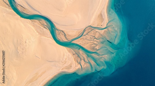 Aerial view of turquoise river delta flowing through desert sand, abstract coastal landscape, turquoise water and beige dunes