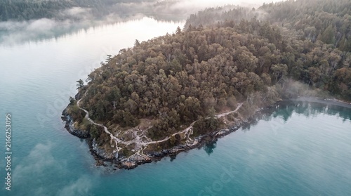 Aerial view of misty forest island, turquoise lake water with morning fog, scenic mountain landscape for travel and nature backgrounds