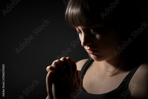 Obraz na plátně Young woman praying with closed eyes in dramatic low light