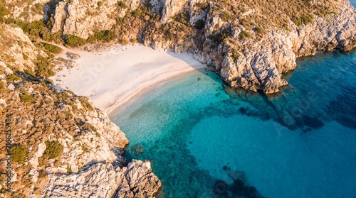 Aerial view of a secluded tropical beach, turquoise ocean water and white sand cove, rocky coastal landscape at sunset
