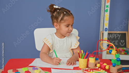 Bild auf Leinwand Little girl drawing with red crayon, right hand on paper at small table in preschool classroom; creative concentration