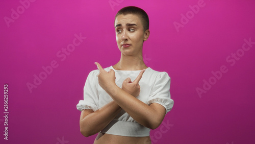 Obraz na płótnie Young woman with short hair in white crop top shows both middle fingers to camera in a pink photo studio, grimacing and shrugging shoulders; defiance attitude