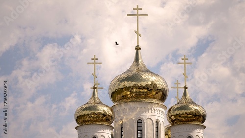 Photography Three golden onion domes topped with orthodox crosses stand against soft blue sky with scattered white clouds