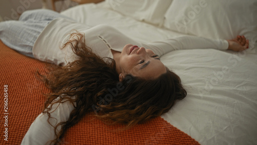 Bild auf Leinwand Woman with arms outstretched beside a standing mirror and bed in a bright bedroom, smiling then reclining on the duvet; joy