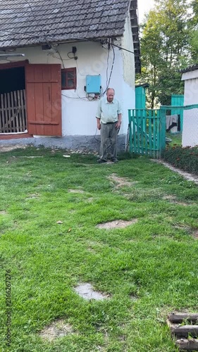 Senior farmer brought a goat from pasture back to a traditional old village barn and sat down to rest in a rural backyard