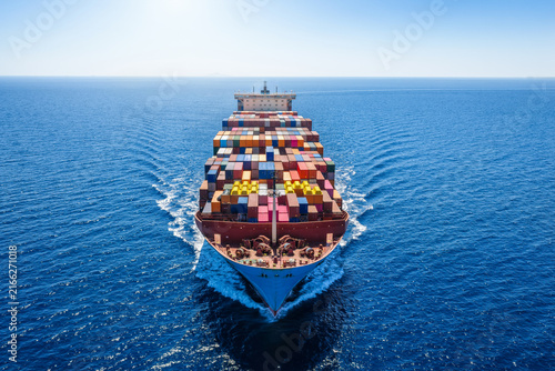 Aerial front view of a heavy loaded, large super cargo container ship sailing over the ocean