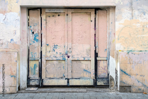 Fotografie Weathered, pale pink double wooden door with peeling paint and exposed layers of