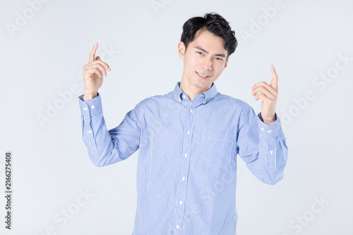Smiling young man pointing upward with both hands in studio