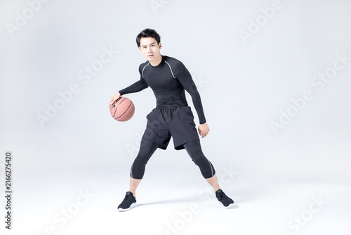 Young male basketball player dribbling ball in studio