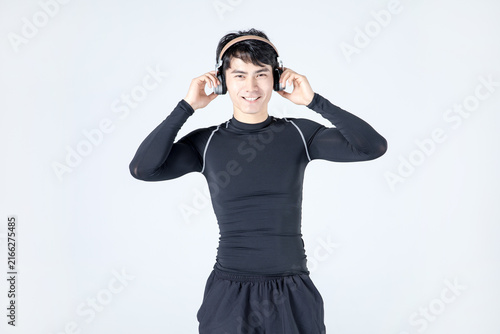 Young athletic man in black sportswear listening to music with headphones