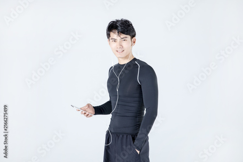 Young athletic man in sportswear listening to music with smartphone on white background