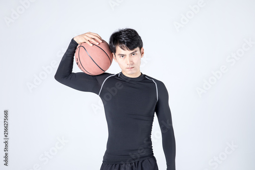 Young male basketball player posing with ball on shoulder in studio