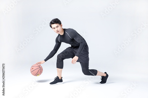 Young man dribbling basketball in studio sportswear