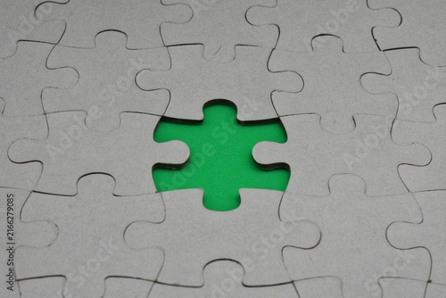 A cardboard jigsaw puzzle with one missing piece revealing a bright green surface underneath.
