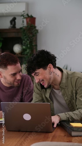 Two young male partners working from home on a laptop, one is on a business phone call