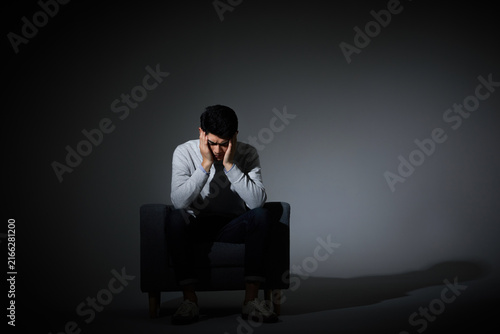 Cuadro en lienzo Depressed young man sitting alone with head in hands in dark room