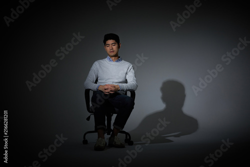 Foto Young man sitting alone under spotlight with shadow in dark studio