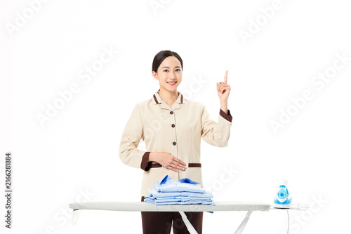 Bild auf Leinwand Smiling housekeeper pointing up beside ironing board with folded laundry