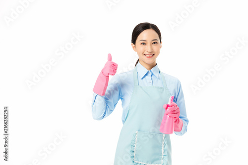 Obraz na plátně Smiling female housekeeper with spray bottle showing thumbs up on white backgrou