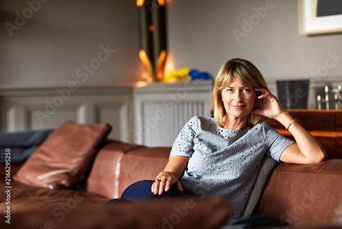 Wellness, calm and woman on sofa with portrait, positive attitude and weekend break with unwind. Wellbeing, space and mature person in house with happy moment, good mood and satisfaction on day off.