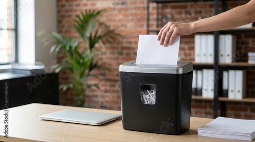 A person's hand using a document shredder to destroy sensitive paper in a modern office setting.