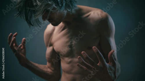 awareness of one's strength Shirtless muscular gray-haired man posing dramatically with raised hands against a dark background, showcasing power and expressive movement