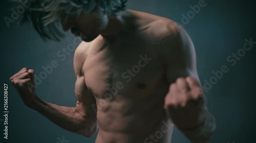 strength invincibility determination Muscular man with long hair posing with clenched fists against a dark textured background, low-key lighting emphasizing fitness, strength, and determination