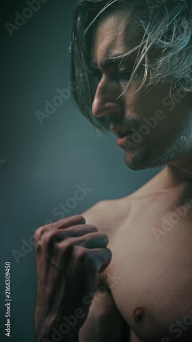 fist will power strength Close-up portrait of a shirtless man with shoulder-length hair and defined muscles, featuring a clenched fist in low-key lighting with dramatic shadows