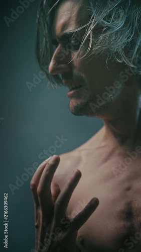 pain suffering tension struggle with oneself profile of a shirtless adult man with long messy hair, expressing intense emotion with clenched fists against dark moody background soft dramatic lighting