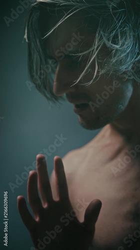 internal stress Close-up portrait of a young adult man with long disheveled hair, showing intense emotion and contemplative hand gestures in moody low-key lighting