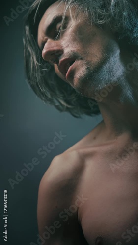 immersion in oneself shirtless young man with long tousled hair in a contemplative pose against dark background, soft directional lighting highlighting skin texture and profile
