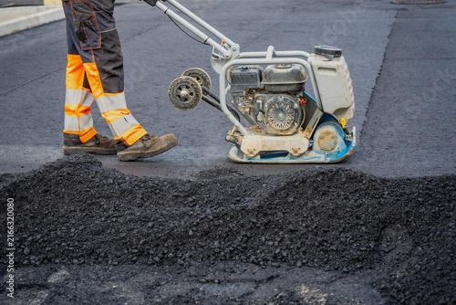 Canvas Print Construction worker operating plate compactor machine on fresh asphalt pavement