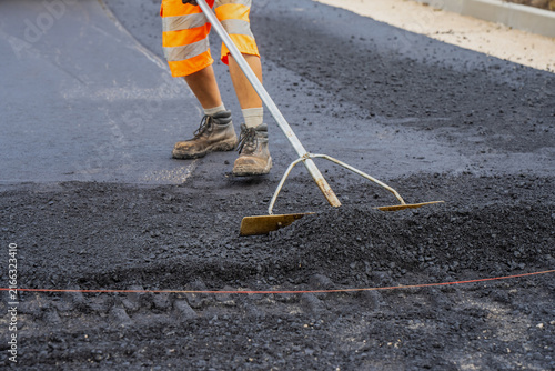 Foto Construction worker using long handled asphalt lute to manually level hot mix as