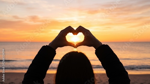 Hands making heart shape framing the sun at sunset on beach, love and romance, summer vacation holiday lifestyle, couple relationship symbol against ocean horizon