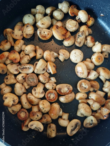 Fotografía Button mushrooms sauté with herbs in a black frying pan, developing a golden brown surface during homemade meal preparation