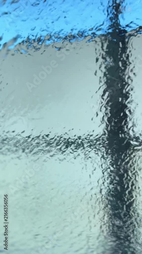 A high-pressure water sprayer rinses a vehicle windshield from the outside, creating streams of flowing water and distorted reflections seen from the car's interior.