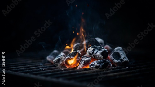 Hot burning charcoal briquettes with glowing amber on outdoor barbecue grill ready for cooking.