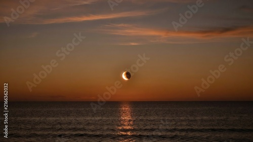 Lunar eclipse crescent moon glows bright over calm dark ocean surface at twilight hour view.