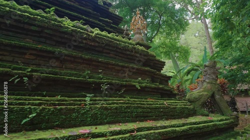 Ancient moss covered Buddhist stupa at tropical forest, Historic Wat Phra Lat temple pagoda with stone guardian sculptures in lush jungle landscape, Chiang Mai, Thailand 4k