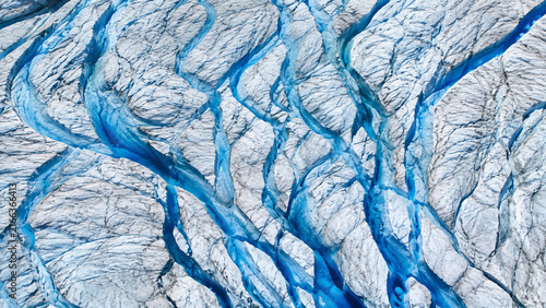 A detailed top-down view reveals deep blue fissures winding through the rough, white surface of a massive glacier.