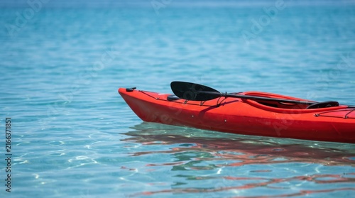 Close-up of an empty red kayak with a black paddle resting on top, floating on clear calm turquoise water