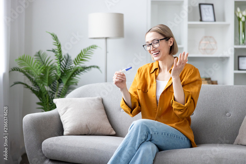 Foto Happy woman sitting on a couch at home, holding a positive pregnancy test and ex