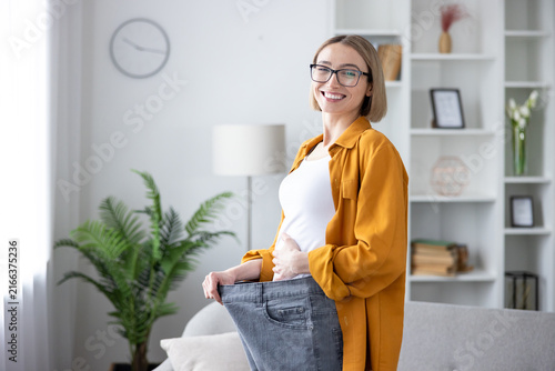Fotografía Happy woman holding up her loose jeans, celebrating successful weight loss and h