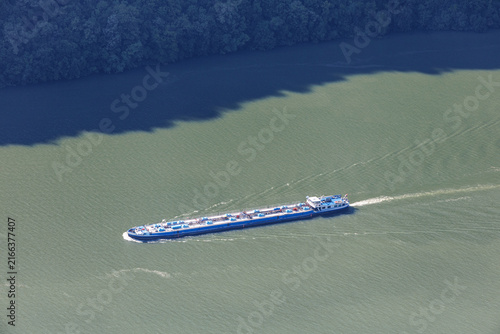 Konstfotografi Aerial top-down view of a blue inland tanker barge navigating a wide green river, leaving a wake