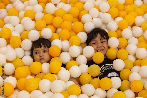 Two happy Asian children having fun in a colorful yellow and white ball pit.