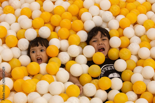 Two Happy Asian Children Having Fun Submerged in Yellow and White Ball Pit