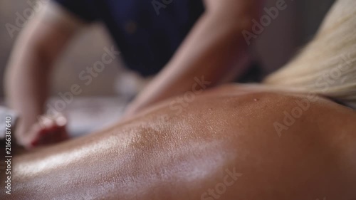Soft focused closeup of woman's oiled back during massage. Warm skin tones, gentle lighting, blurred therapist hands in background. Evokes calm, luxury, wellness