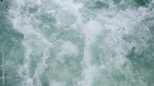 Close up top view of turbulent blue ocean water with white foam and bubbles. Powerful churning sea waves creating a textured splashing pattern. Nature background of rushing river or boat wake.